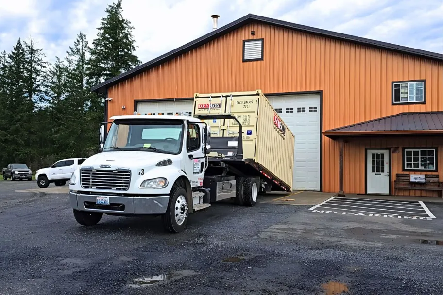 A Dry Box tilt-bed delivery truck carrying a shipping container