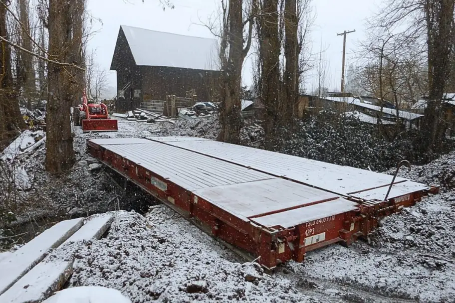 A flat rack container used as a bridge in a snowy rural yard