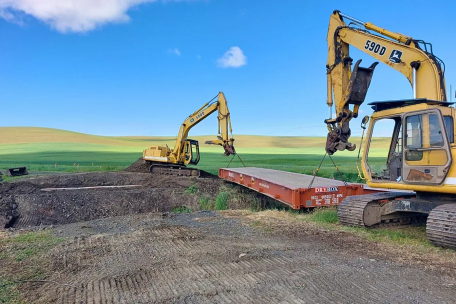 Excavators positioning a flat rack container to build a bridge