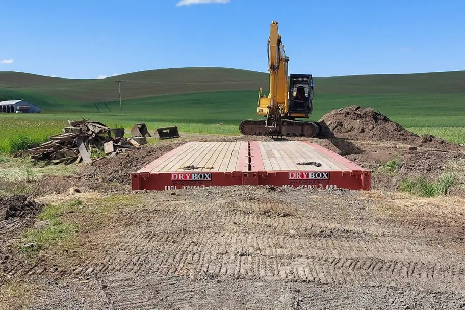 An excavator on a long flat rack container bridge in open farmland