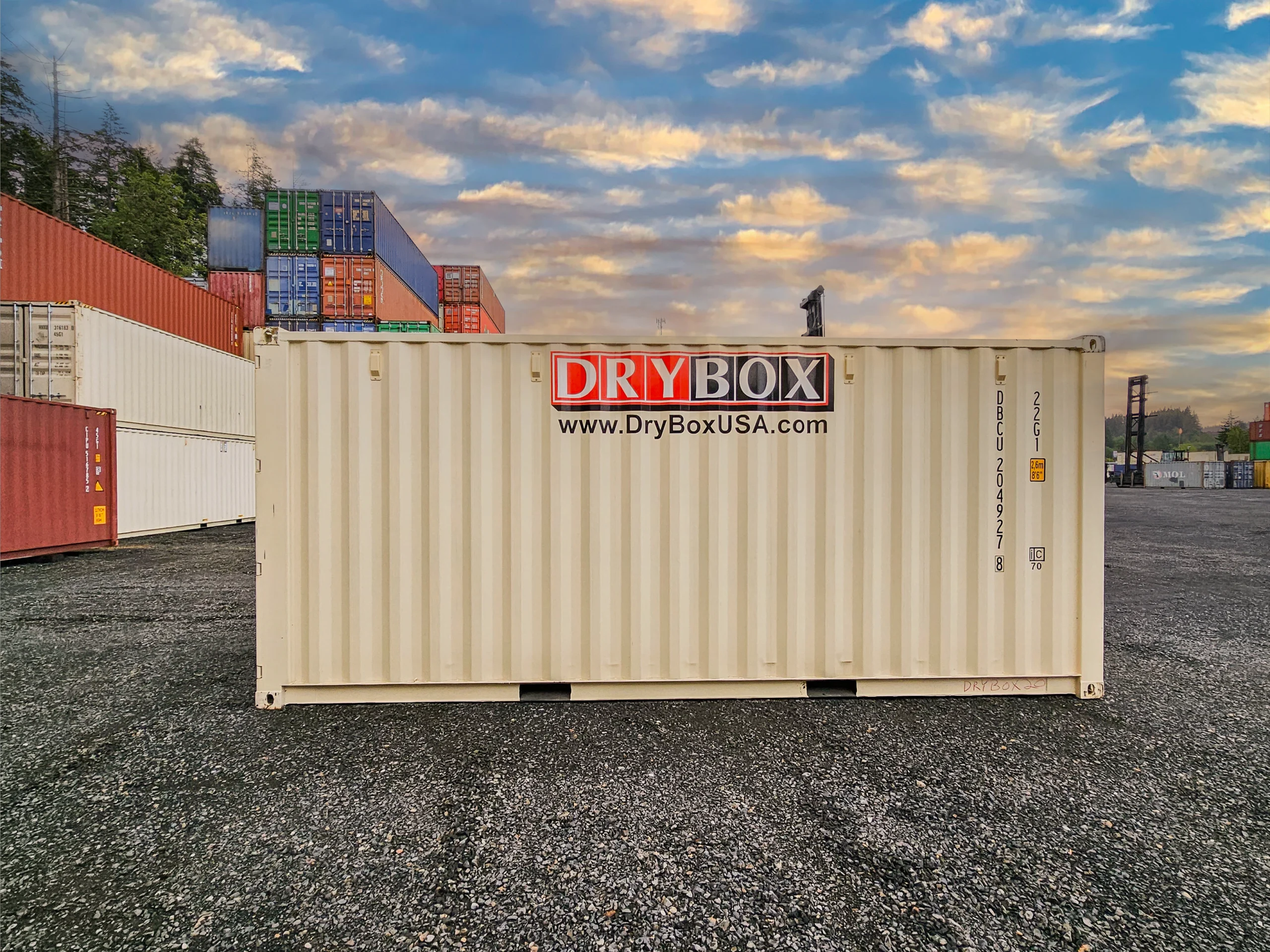 A twenty-foot long, beige shipping container, on gravel.