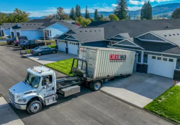 A truck delivers a portable storage container in a driveway.
