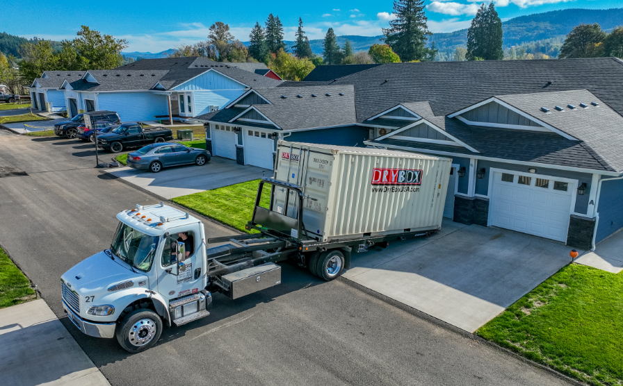 A truck delivers a portable storage container in a driveway.